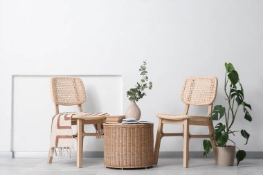 Sandalyeler, dekorlu sepet ve beyaz duvarın yanındaki ev bitkisi.