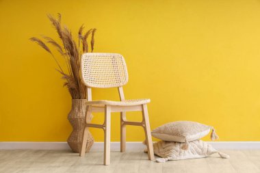 Sandalye, vazodaki otlar ve odadaki sarı duvarın yanındaki minderler.