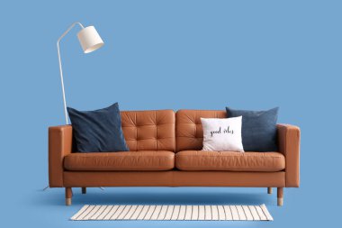 Mavi arka planda yastıkları ve lambası olan rahat bir kanepe.