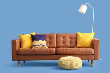 Mavi arka planda rahat bir kanepe, lamba ve puf.