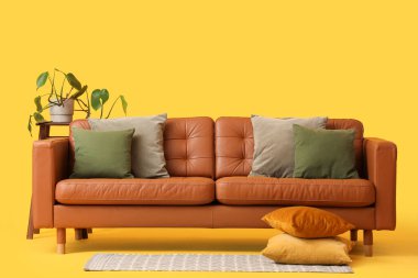 Konforlu kanepe, çiçek ve yerde sarı arka planda yastıklar.