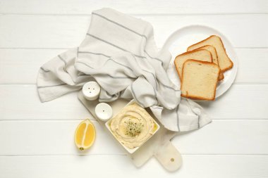 Beyaz ahşap arka planda mikro yeşil, limonlu ve kızarmış ekmekli lezzetli humus kasesi.