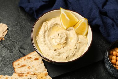 Limonlu bir kase lezzetli humus ve siyah grunge arka planda gevrek.