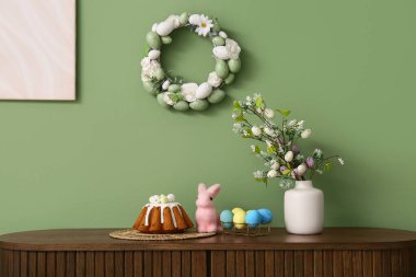 Ağaç dalları olan vazo, Paskalya pastası, yumurta ve tavşan yeşil duvarın yanında.