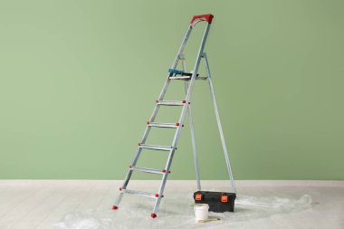 Odada yeşil duvarın yanında boya aletleri olan merdiven.