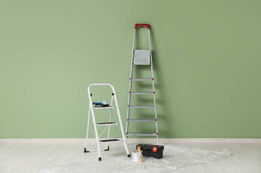 Odada yeşil duvarın yanında boya aletleri olan merdivenler.