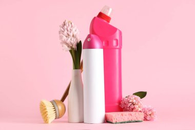 Pembe arka planda bahar çiçekleriyle temizlik malzemeleri.