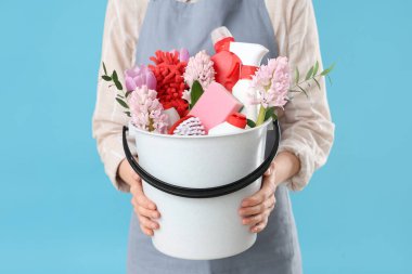 Temizlik malzemeleri ve mavi arka planda bahar çiçekleri olan kadın hademe, yakın plan.