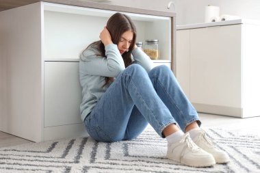 Genç bir kadın mutfakta yerde panik atak geçiriyor.