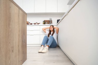 Genç bir kadın mutfakta yerde panik atak geçiriyor.