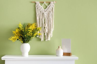 Mimoza çiçekli vazo ve şömine rafında yeşil duvarın yanında.