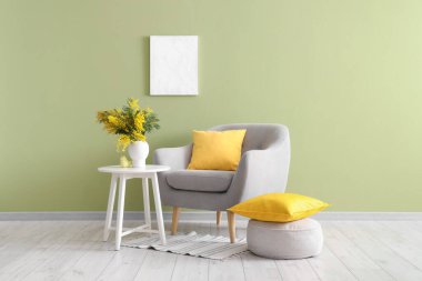 Oturma odasının içinde vazoda koltuk, masa ve mimoza çiçekleri var.