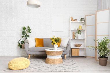 Oturma odasının içinde kanepe, raf ünitesi ve vazoda mimoza çiçekleri var.