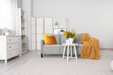 Oturma odasının içinde kanepe, katlanan perde ve vazoda mimoza çiçekleri var.