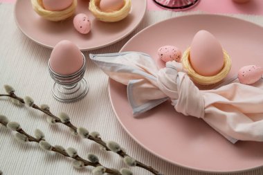 Beautiful table setting with Easter eggs and pussy willow branches on pink background, closeup