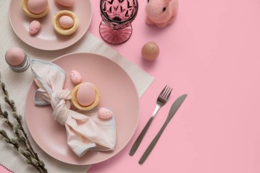 Beautiful table setting with Easter eggs, toy bunny and pussy willow branches on pink background