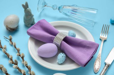 Beautiful table setting with Easter eggs, toy bunny and pussy willow branches on blue background, closeup