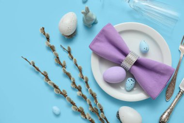 Beautiful table setting with Easter eggs, toy bunny and pussy willow branches on blue background