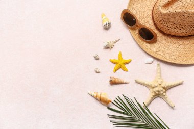 Güneş gözlüklü yaz şapkası, palmiye yaprağı ve pembe grunge arka planda deniz kabukları