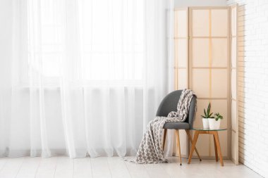 Koltuk, masa ve katlanan ekran, odada ışık perdesinin yanında.