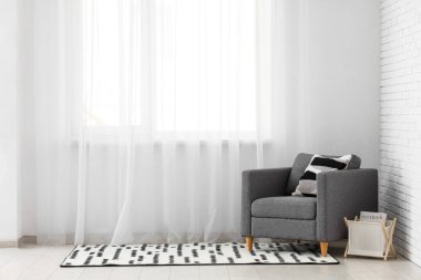 Koltuk ve dergi standı ve halı odada ışık perdesi yanında.