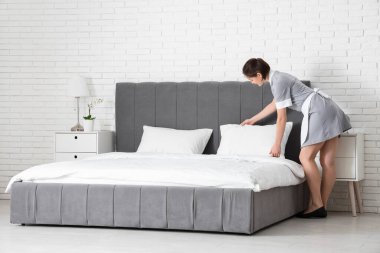 Genç oda hizmetçisi otel odasında yastığı ayarlıyor.