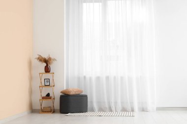 Odadaki ışık perdesinin yanındaki raf üniteli Pouf.