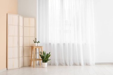 Odadaki ışık perdesinin yanında bitkilerle ve katlanan perdeyle dışkı