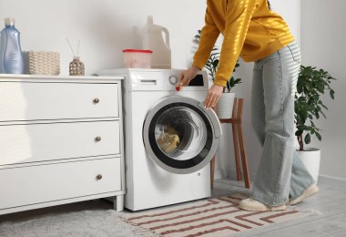 Kadın çamaşır makinesine çamaşır deterjanı koyuyor.