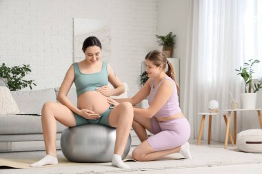 Hamile bir kadınla evde fitbol antrenmanı yapan genç bir doula.