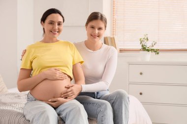 Genç doula ve hamile kadın yatak odasında oturuyor.