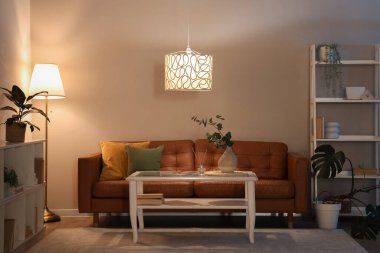 Konforlu kanepe, kahve masası ve geceleri oturma odasının içinde parlayan lambalar.