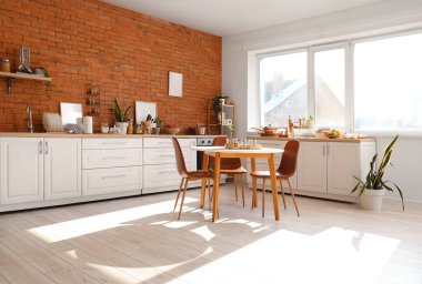 Mutfağın içinde tezgahlar, yemek masası ve çatal bıçaklar var.