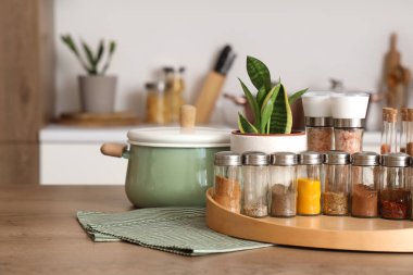 Farklı baharatlı kavanozlar, mutfak masasında tencere ve bitki.