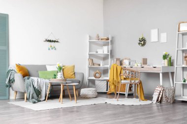 Paskalya için dekore edilmiş oturma odasının içinde çalışma yeri, raf üniteleri ve kanepe var.