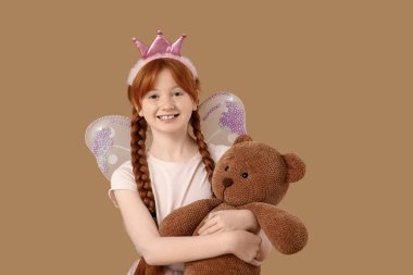 Kahverengi arka planda oyuncak ayısı olan sevimli kızıl saçlı peri.