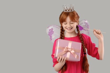 Gri arka planda sihirli değneği ve hediye kutusuyla peri gibi giyinmiş tatlı kızıl kız.