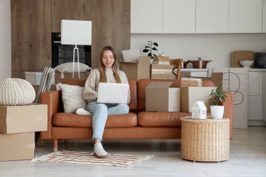 Taşınırken mutfakta dizüstü bilgisayar kullanan genç bir kadın.