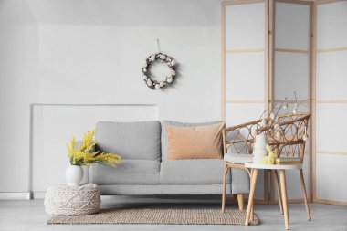 İçinde kanepe, masa ve Paskalya çelengi olan aydınlık oturma odası.