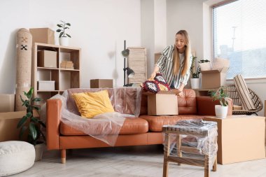 Genç bir kadın taşınma gününde koltuğu kutuya koyuyor.