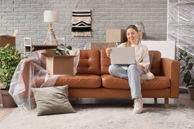 Taşınırken odada dizüstü bilgisayar kullanan genç bir kadın.