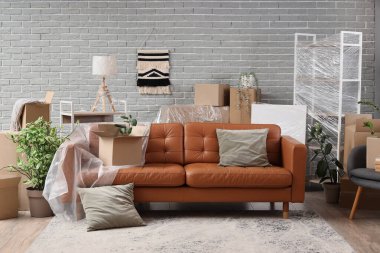 Üzerinde film, yastık ve karton kutular olan kahverengi kanepe taşınma gününde oturma odasında.