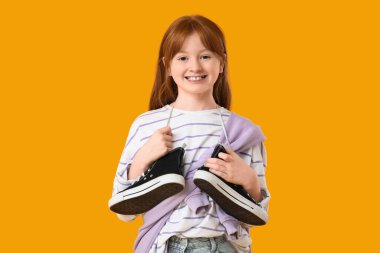 Sarı arka planda spor ayakkabıları olan genç bir kız.