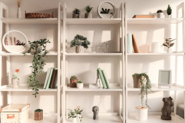 Yapay bitkiler, kitaplar ve ışık duvarı yakınında dekorasyon üniteleri rafa kaldırılıyor.