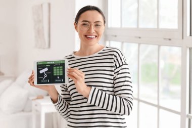 Yatak odasında akıllı ev güvenlik sistemi kontrol paneli olan genç bir kadın var.