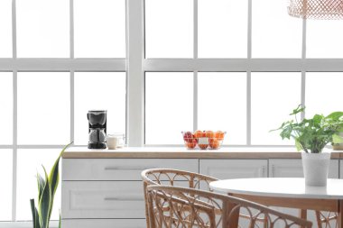 Beyaz tezgahlı, yemek masalı ve büyük pencereli aydınlık mutfağın içi.