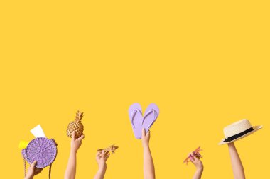 Birçok el sarı arka planda farklı plaj aksesuarlarını tutuyor.