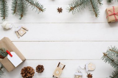 Noel ağacı dallarından yapılmış bir çerçeve koni ve beyaz ahşap arka planda hediye kutuları.