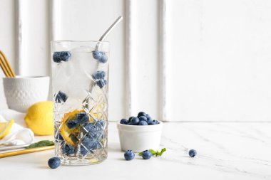 Bir bardak taze yabanmersinli limonata ve beyaz arka planda böğürtlenli kase.