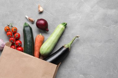 Gri arka planda içi taze sebzelerle dolu kağıt torba.